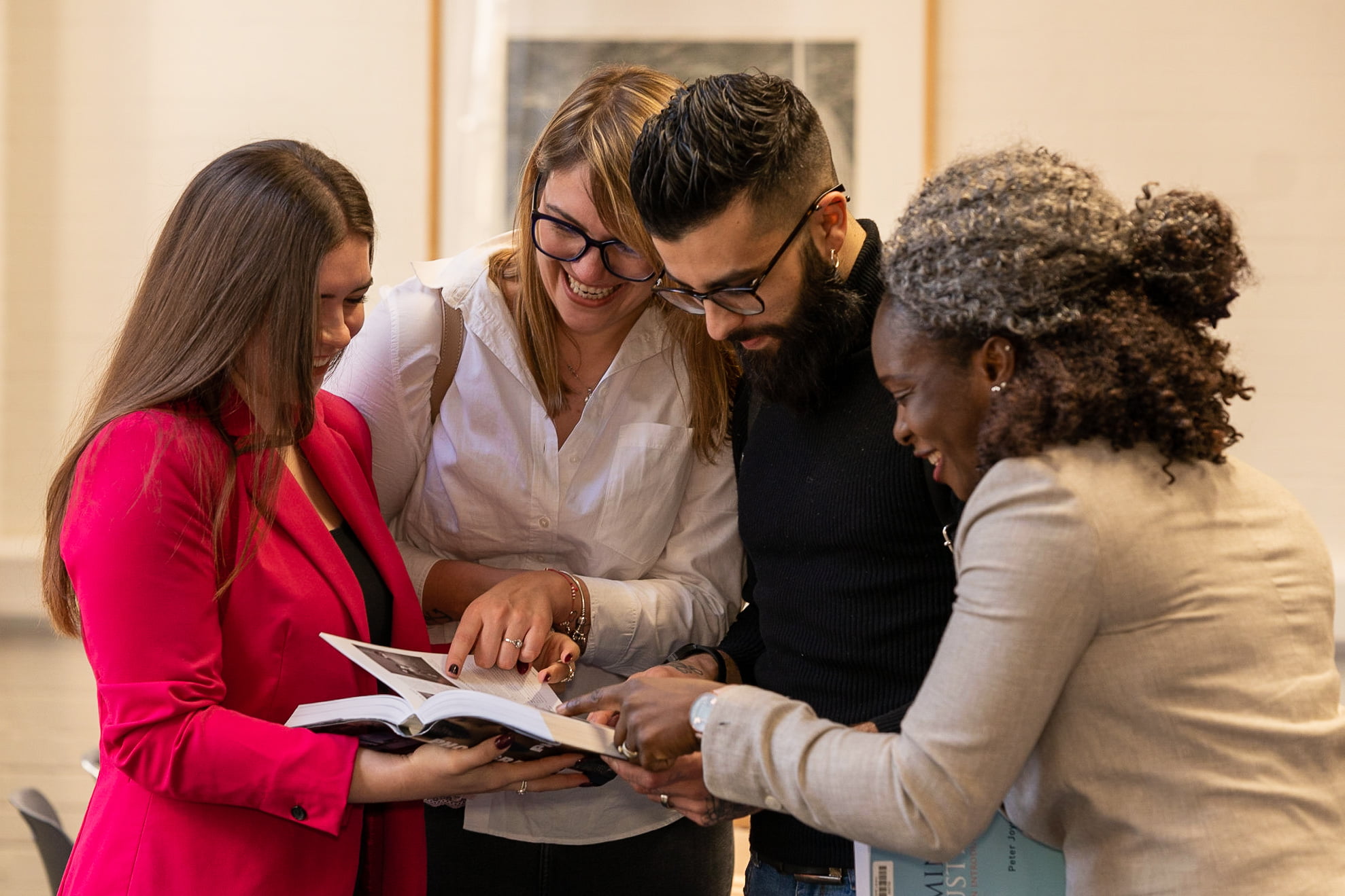 A group of people standing around each other look at a book simultaneously.