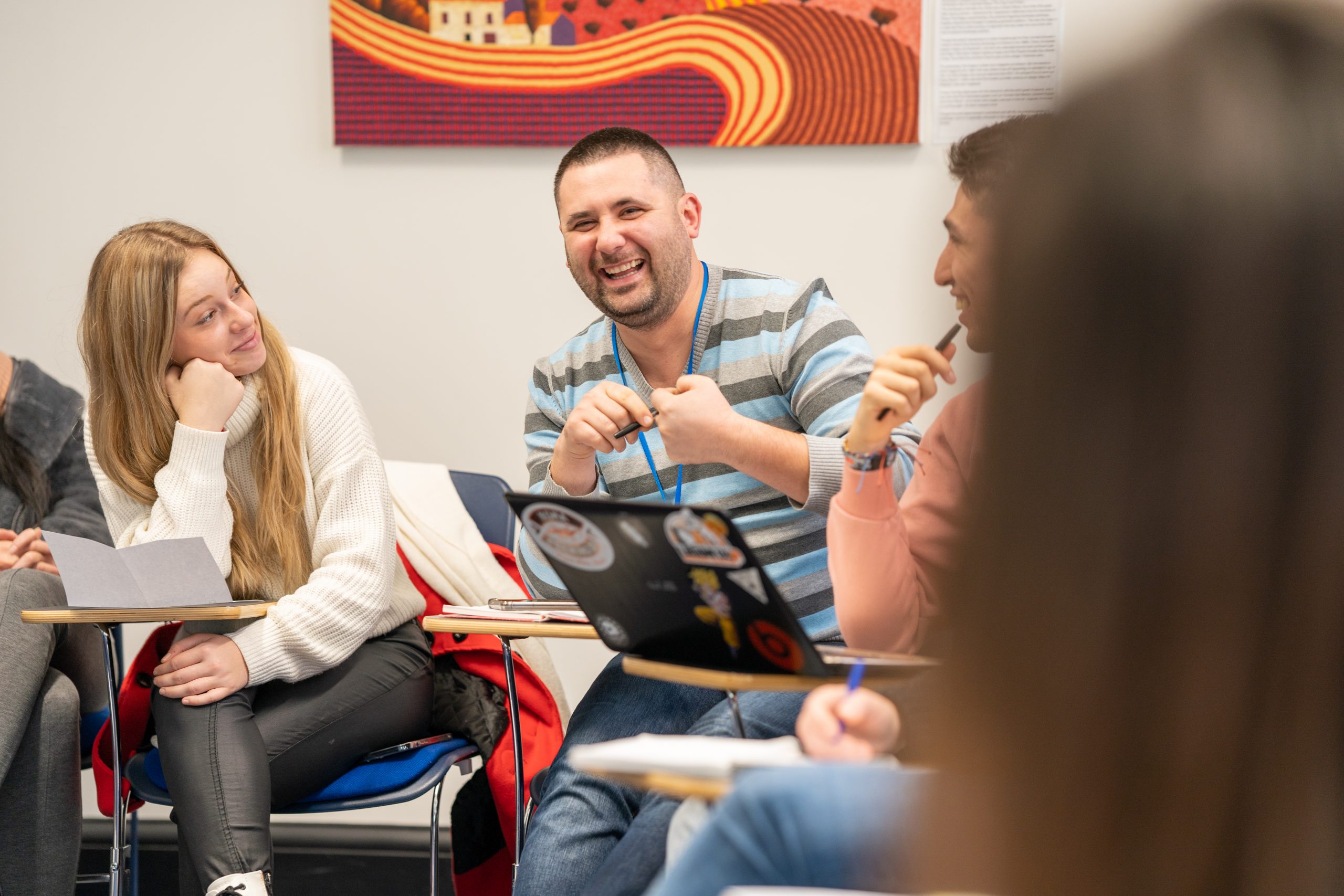 A group of people sitting around a laptop computer. They are all sitting on classroom chairs.