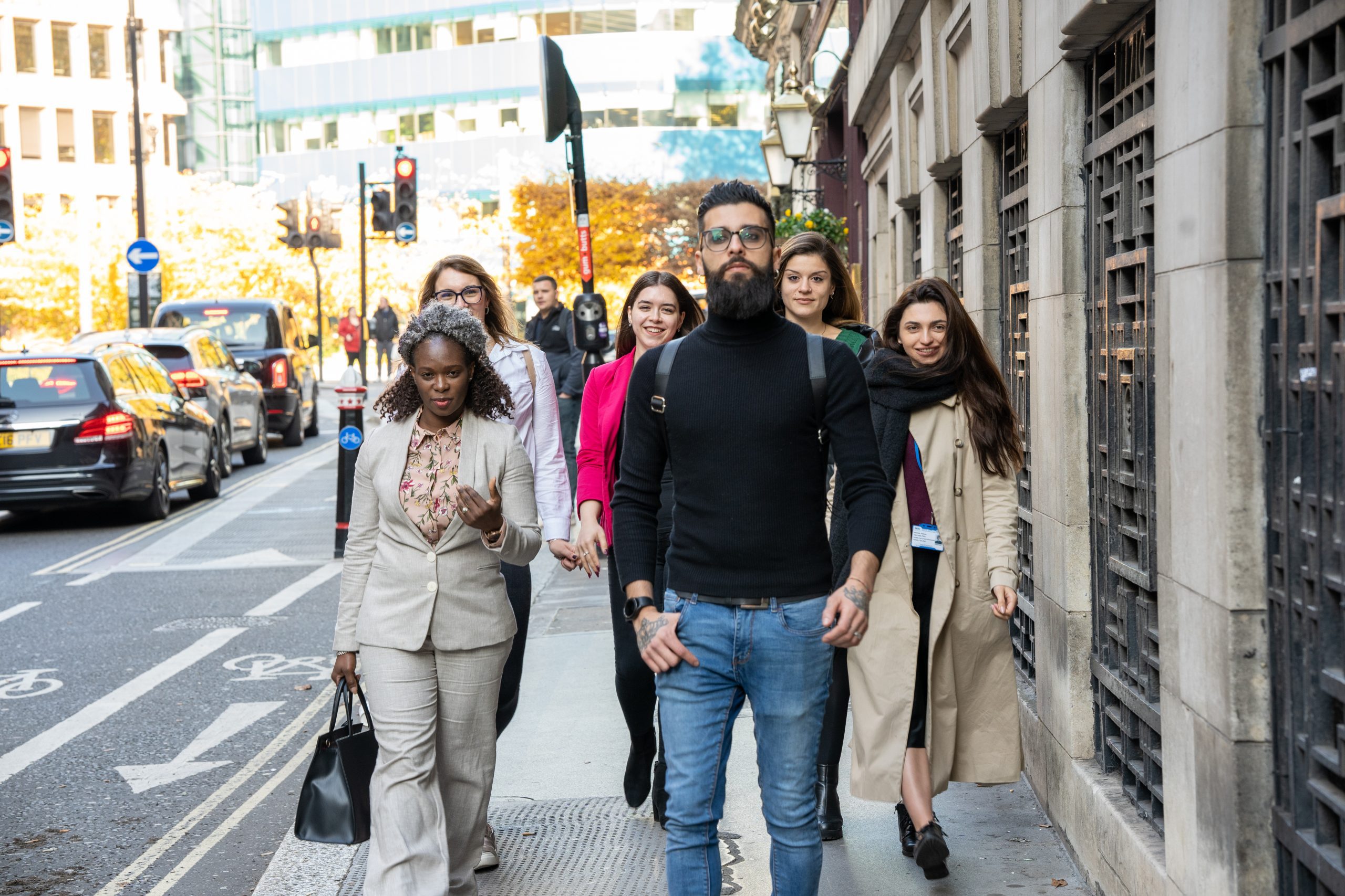 A large group of people walk down a busy London City street. They are heading to the DGHE building.